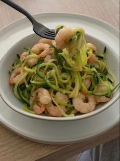 a white bowl filled with zucchini noodles and shrimp on top of a wooden table