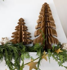 three cardboard christmas trees on top of a mantel with greenery and gold stars