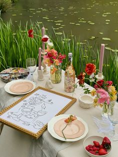 the table is set with plates, bowls and vases on it next to water