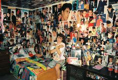 a woman sitting on top of a bed next to a wall covered in pictures and posters