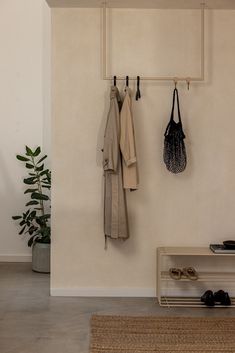 a coat rack with two coats hanging from it's hooks and some shoes on the floor