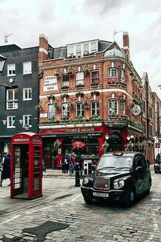 a black car driving down a street next to tall brick buildings and red telephone booths