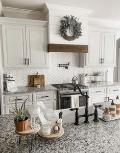 a kitchen with white cabinets and marble counter tops, black faucet, potted plants on the stove