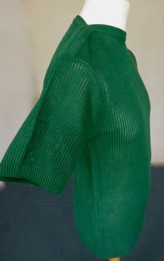 a mannequin wearing a green sweater on a white display stand in front of a wall