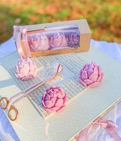 some pink flowers are on top of a white table cloth with scissors and paper clips