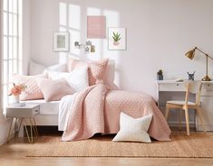 a bed with pink comforter and pillows in a room next to a desk, chair and window