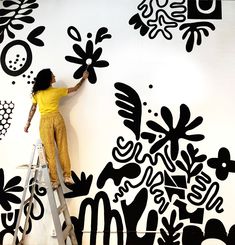 a woman on a ladder painting a wall with black and white designs