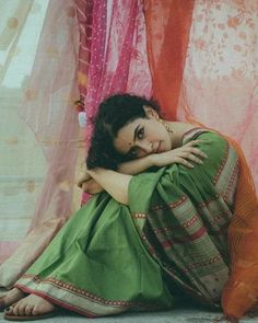 a woman is sitting on the ground with her arms folded over her head and looking at the camera