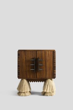 a small wooden cabinet with two tassels on the legs and one drawer open