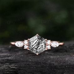 an engagement ring with three diamonds on top of a piece of wood in front of some trees