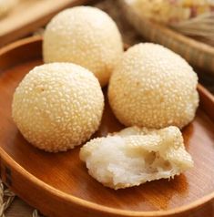 three sesame balls on a wooden plate with rice in the bowl next to it and a woven basket behind them