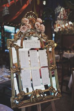 an ornate gold framed mirror with seating cards on the front and side, sitting on a table at a wedding reception