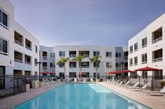 an empty swimming pool with lounge chairs and umbrellas in front of the apartment buildings