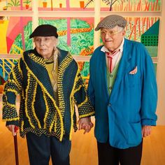 an older man and woman standing next to each other in front of colorful paintings on the wall