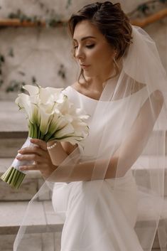 a woman in a white dress holding a bouquet of flowers and wearing a veil over her head