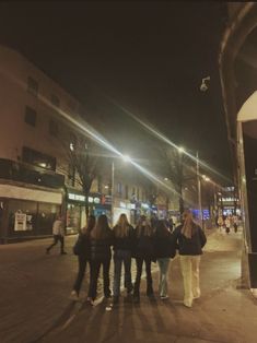 a group of people standing in the middle of a street at night time with their backs turned to the camera