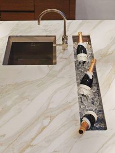 two bottles of wine sitting on top of a marble countertop next to a sink