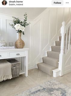 a vase with flowers sitting on top of a white table next to a stair case