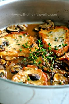 a pan filled with meat and mushrooms covered in gravy, garnished with fresh herbs