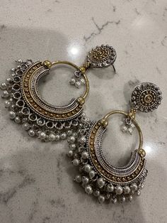 Beautiful pair of chandbali earrings with pearls dangling at the bottom. The earrings are dual tone with silver and gold polish finish. Note that all elements in this set are not precious. Premium dual tone chandbali earrings | indian jewelry online shopping usa | chandbali earrings online | pearl earrings | pearl chandbalis Cheap Bohemian Chandbali Danglers, Gold Dual-tone Chandbali Earrings, Pearl Drop Chandbali Earrings, Chandbali Pearl Drop Earrings, Dual-tone Chandbali Earrings For Festive Occasions, Silver Dual-tone Temple Jewelry Chandbalis, Silver Dual-tone Temple Chandbalis, Silver Chandbali Chandelier Earrings With Pearl Drop, Festive Dual-tone Chandbali Earrings