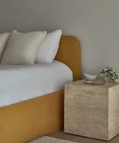 a bed with white sheets and pillows next to a small table on top of it