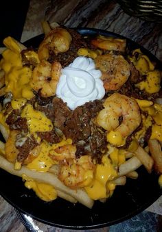 a black plate topped with french fries covered in cheese and meats next to sour cream