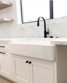 a white kitchen with marble counter tops and black faucet, along with open shelving