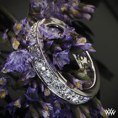 two wedding rings sitting on top of purple flowers with diamonds in the middle and bottom