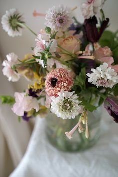 a vase filled with lots of flowers on top of a white cloth covered tablecloth