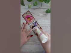 a woman is holding an empty tube in her hand and some flowers are on the table