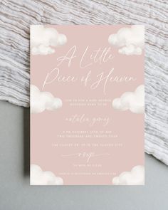 a pink and white wedding card with clouds in the sky, on top of a blanket