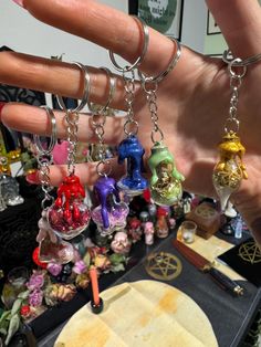 a hand is holding several charms in front of a table full of other jewelry items