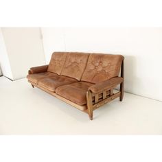 a brown leather couch sitting on top of a white floor next to a wooden frame