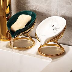 two white and gold bowls sitting on top of a counter next to a golden faucet