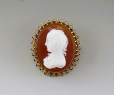 Presented is an antique, Victorian, 10 karat yellow gold and hand carved hard stone cameo pin or brooch made during the second half of the 1900s. This piece is done in a classic form and shows a portrait of a lovely woman. The 10 karat gold mounting has secure prongs and the back of the pin has a replacement C style clasp. This piece has been tested and is guaranteed to be 10 karat gold purity. This piece is in excellent overall condition. Length: 1 1/8 inches. Weight: 5.3 grams. Classic Gold Brooch With Intaglio Detail, Classic Gold Intaglio Brooch, Classic Gold Intaglio Brooches, Classic Gold Brooches With Intaglio, Heirloom Yellow Gold Cameo Brooches, Victorian Cameo Brooches In Yellow Gold, Victorian Cameo Brooch In Yellow Gold, Victorian Yellow Gold Cameo Brooches, Antique Oval Cabochon Brooch For Formal Occasions