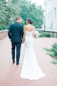 a bride and groom walking down a brick walkway holding hands in front of a building