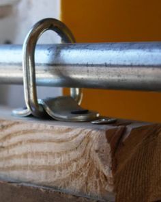 a close up of a metal handle on a wooden beam with a yellow wall in the background