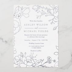 a wedding card with flowers and leaves on the front, in grey ink against a white marble background