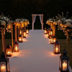 A wedding ceremony aisle lined with vintage lanterns, some glowing with candles, others filled with flowers, casting a warm, romantic light across the path leading to the altar. Lantern Pathway Wedding, Lanterns Lining Wedding Aisle, Lanterns For Wedding Aisle, Candle Aisle Wedding Outdoor, Enchanted Indoor Wedding, Blue And Black Theme Wedding, Unique Aisle Runner, Vintage Wedding Aisle Decorations, Lanterns Down The Aisle Wedding