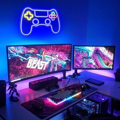 two computer monitors sitting next to each other on top of a desk in front of a neon sign