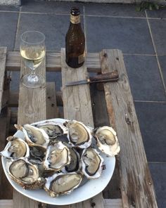 a plate of oysters on a wooden table next to a wine glass and bottle