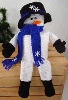 a crocheted snowman wearing a hat, scarf and mittens on a wooden crate