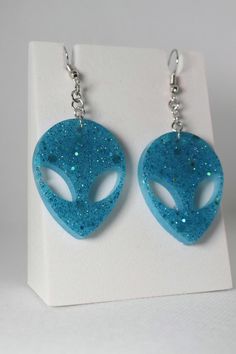 Let your unique style take flight with these stylish and eye-catching Alien Head Earrings! Add an other-worldly touch to any look with these intricately designed and handmade earrings. Crafted from epoxy resin, the sparkly multi-option background gives off a dazzling effect that's sure to get you noticed. Meanwhile, the glitter adds extra dimension and a pop of color that will make it hard for people not to stare. Whether you prefer a bold, vibrant style or something more subtle, these Alien Hea Space-themed Dangle Jewelry Gift, Hypoallergenic Resin Jewelry For Parties, Handmade Space-themed Earrings For Gift, Handmade Space-themed Earrings As Gift, Novelty Resin Dangle Jewelry, Novelty Drop Earrings For Party, Novelty Blue Drop Earrings, Handmade Space-themed Dangle Jewelry, Adjustable Resin Teardrop Jewelry