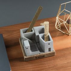 a wooden desk with a laptop, pencil holder and pen on it next to a model house