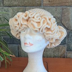 a white mannequin head wearing a crochet hat on top of a wooden table