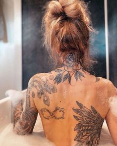 a woman with tattoos on her back sitting in a bathtub