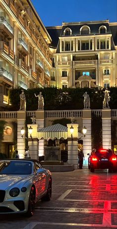 two luxury cars parked in front of a hotel at night with red lights on the street