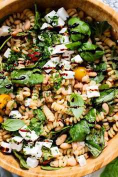 a wooden bowl filled with pasta salad on top of a table