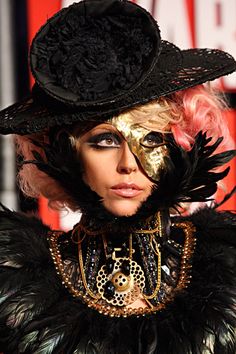 a woman with pink hair wearing a black hat and feathered dress is posing for the camera