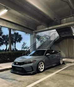 a gray car parked in a parking lot next to stairs and palm trees on the other side